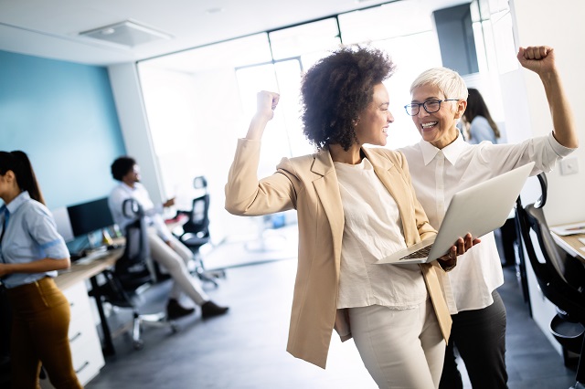 Para-montar-uma-agência-de-marketing-digital-é-preciso-dedicar-se-A-foto-mostra-duas-mulheres-de-diferentes-idades-vibrando-enquanto-trabalham